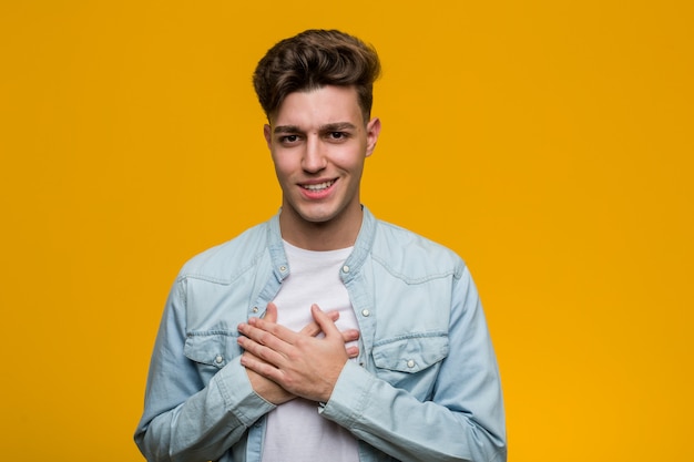 Young handsome student wearing a denim shirt has friendly expression, pressing palm to chest. Love concept.