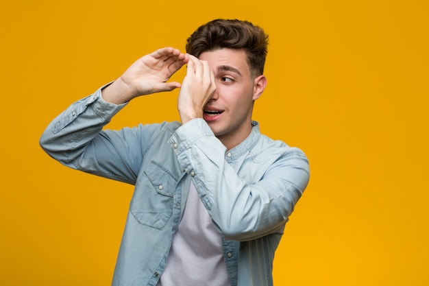 Young handsome student wearing a denim shirt looking far away keeping him hand on forehead.