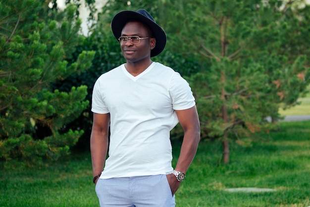 A young and handsome stylish model afro- american man in a stylish suit white t-shirt and a black hat in a summer park . latino american hispanic businessman black guy posing at photoshoot
