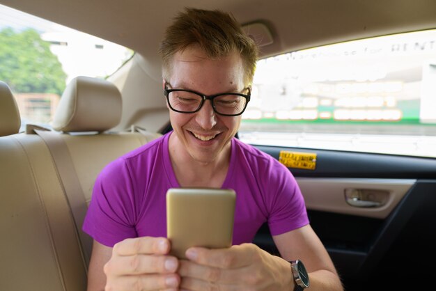 Фото Молодой красивый туристический человек с помощью телефона на заднем сиденье автомобиля