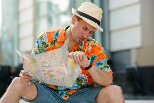 Young handsome tourist man with map checking the time in the city outdoors