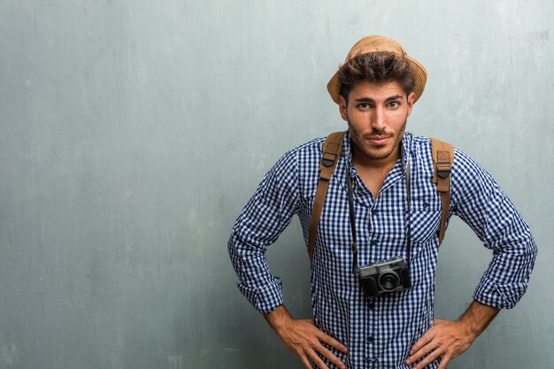 Photo young handsome traveler man wearing a straw hat, a backpack and a photo camera very angry and upset