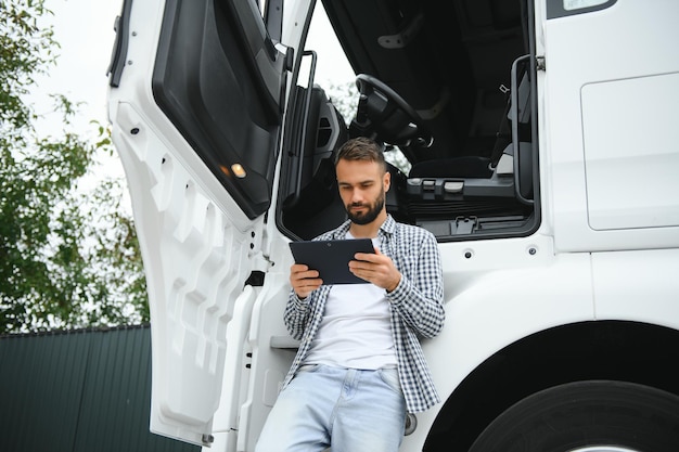 Photo young handsome truck driver is standing with a tablet near the truck