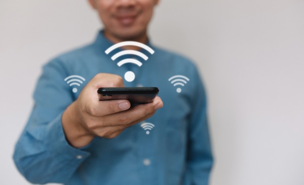 밝은 파란색 셔츠를 입은 젊은 미남은 Wi-Fi 기술에 연결된 스마트폰을 사용합니다.