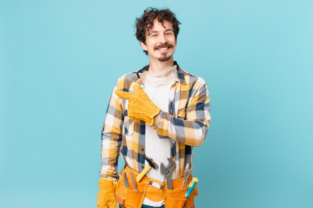 Young handyman housekeeper smiling cheerfully, feeling happy and pointing to the side