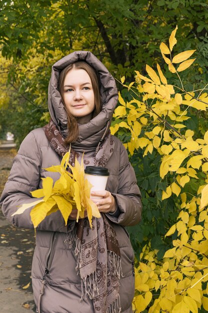 コーヒーと黄色の葉を持つ若い幸せの美しい少女秋の秋の色