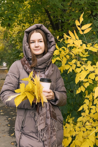 Giovane felicità bella ragazza con caffè e foglie gialle colori della stagione autunnale autunnale