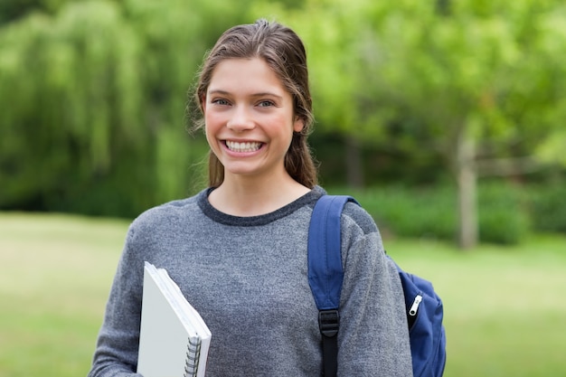 Young happy adult coming back from school while holding a notebook