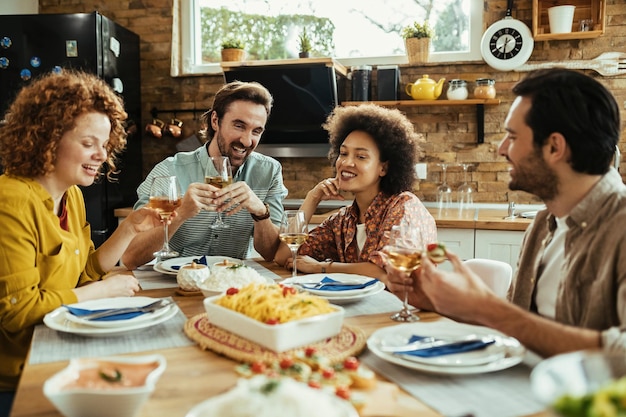 昼食時にダイニングテーブルでワインを飲みながら話している若い幸せな大人