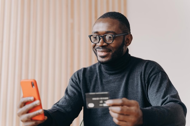 Photo young happy african american male entrepreneur with credit card using ebanking app on smartphone