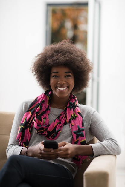 young happy african american woman sitting on sofa and using mobile phone at luxury home