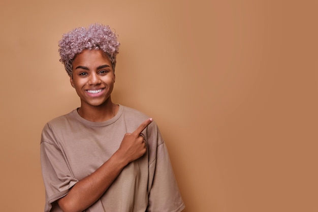Молодая счастливая афро-американская женщина улыбается и показывает рукой на копировальном пространстве