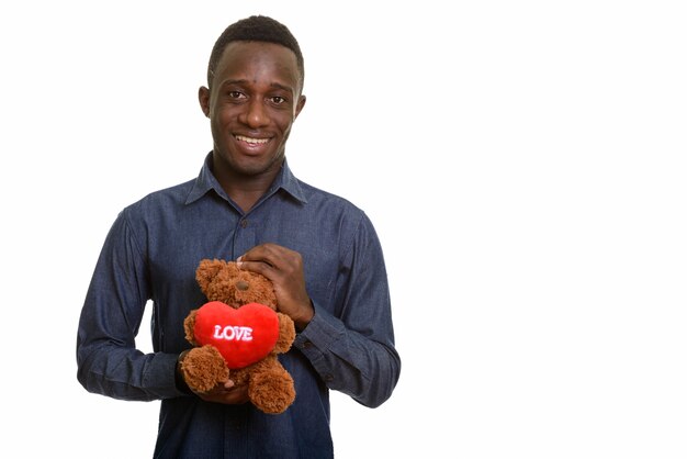 Молодой счастливый африканский мужчина улыбается и держит плюшевого мишку с сердцем