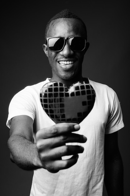 Young happy African man wearing sunglasses and holding heart