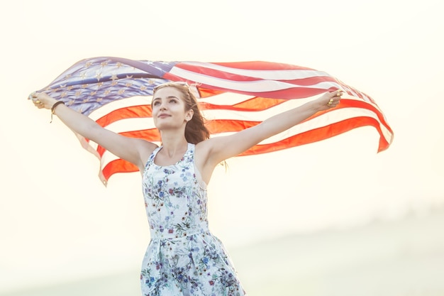 アメリカの国旗を保持している若い幸せなアメリカ人女性。