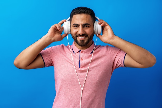 Young happy arab man with headphones listening to music against blue background