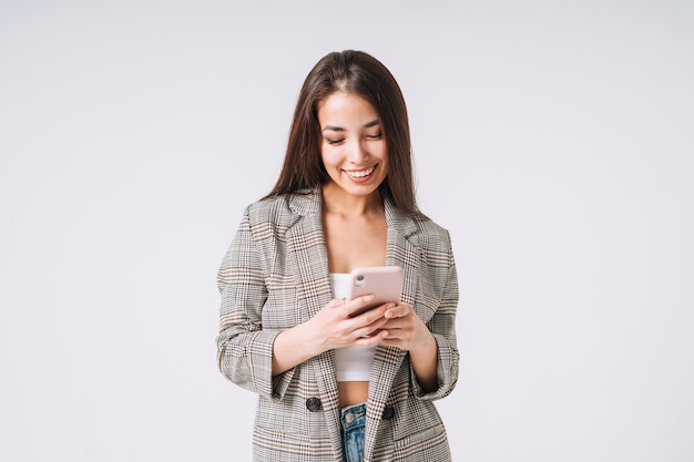 young happy asian business woman with long hair in suit using mobile phone on grey background