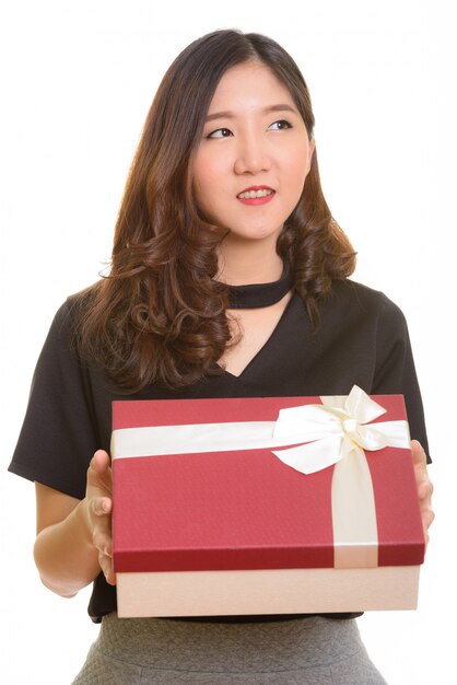 Young happy Asian businesswoman holding gift box while thinking ready for Valentine's day