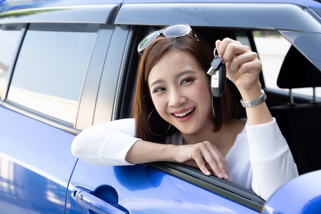 若い幸せなアジア車ドライバーの女性の笑顔と新しい車のキーを示します。初心者ドライバーのコンセプト