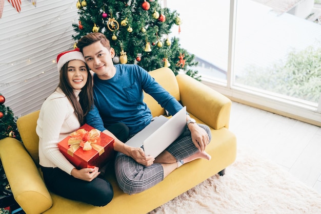 Young happy Asian couple sitting together video call on a laptop with friends or parents thanks for a gift received during the Christmas holiday Celebrate the Boxing day concept