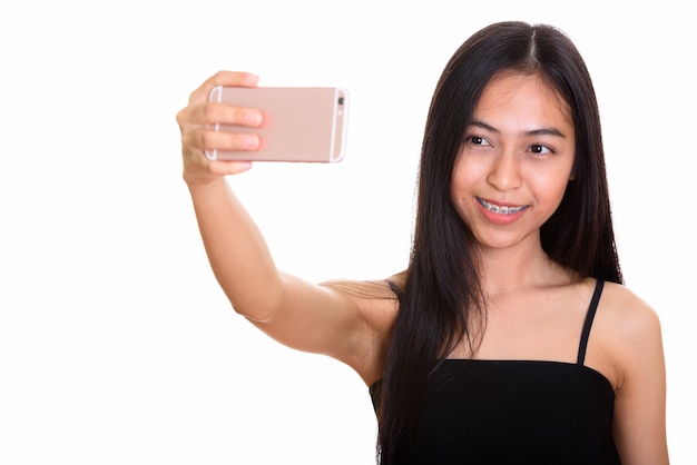 Young happy Asian teenage girl smiling while taking selfie