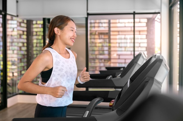 Il giovane atleta asiatico felice della donna funziona sulla macchina da corsa del tapis roulant nella palestra dell'interno fitness per la salute