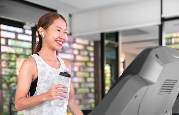 Young happy asian woman athlete run on treadmill running\
machine in indoor gym fitness for health