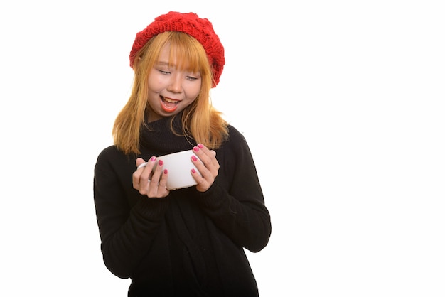 Young happy Asian woman smiling while holding and looking at coffee cup