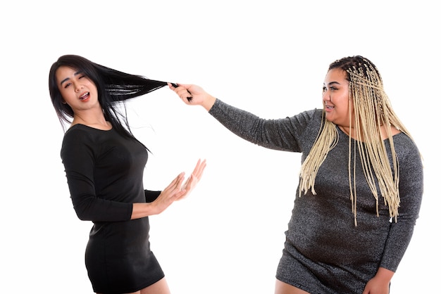 Young happy Asian woman smiling while pulling hair of Asian friend