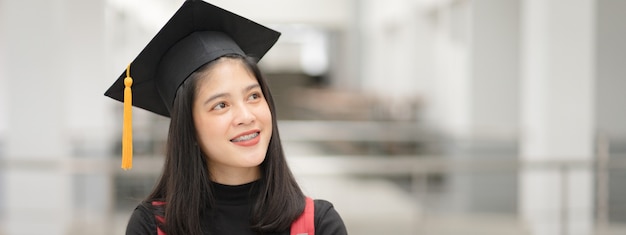 Young happy Asian woman university graduate in graduation gown and cap in the college campus. Education stock photo