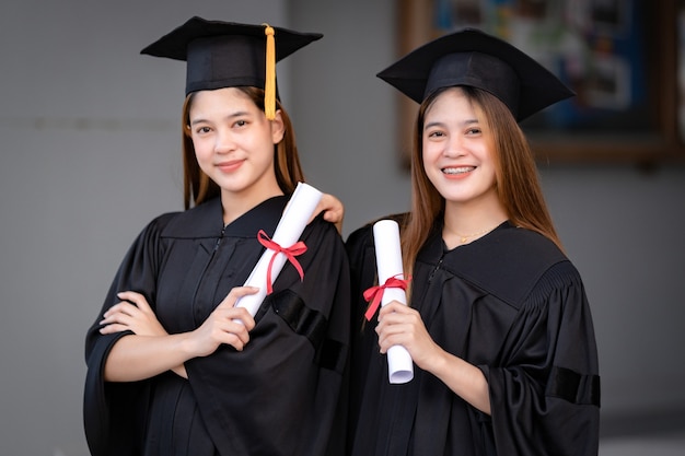 Young happy asian woman university graduates in graduation gown\
and mortarboard hold a degree certificate celebrate education\
achievement in the university campus. education stock photo