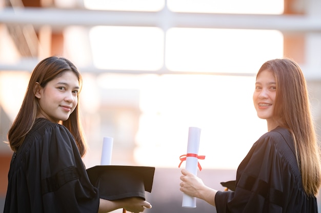 Young happy asian woman university graduates in graduation gown\
and mortarboard hold a degree certificate celebrate education\
achievement in the university campus. education stock photo