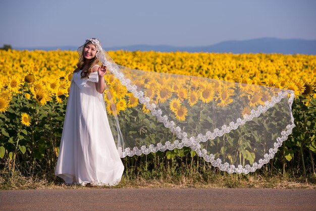 Young happy Asian woman in wedding dress having fun and relax on Sunflower field