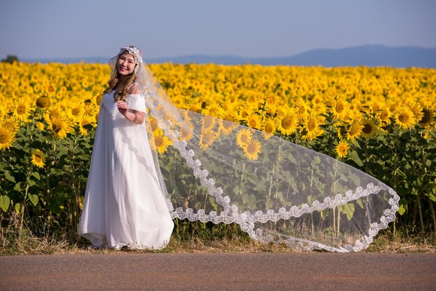 Молодая счастливая азиатка в свадебном платье веселится и отдыхает на подсолнуховом поле