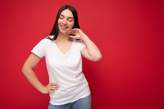 Young happy attractive brunette woman with sincere emotions isolated on background wall with copy space wearing casual white t-shirt for mockup. Positive concept.