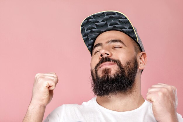 Young happy bearded football fan in cap celebrating. emotional man screaming on pink background