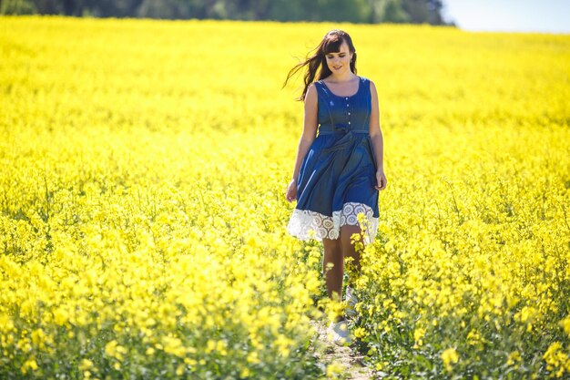 Young happy beautiful big size model girl in blue dress on blooming rapeseed field in summer