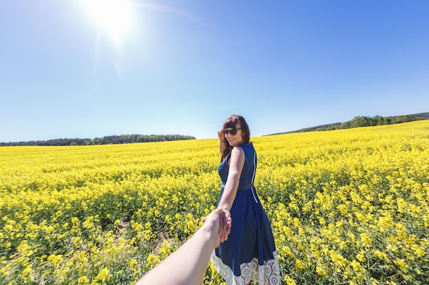 Young happy beautiful big size model girl in blue dress and sunglasses on blooming rapeseed field in summer Follow me concept