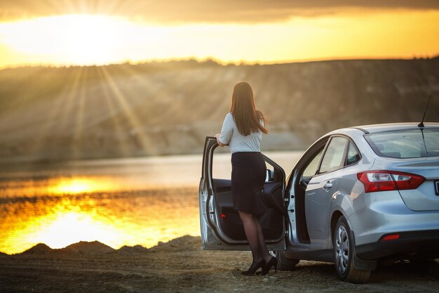 Young happy beautiful big size model girl near her car on sunset business woman resting after a hard day's work