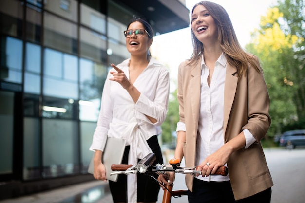 Young happy beautiful businesswomen talking outdoor. Office building on background.