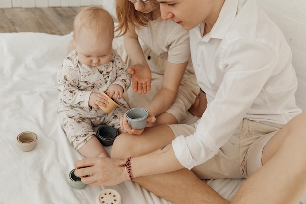 Young happy beautiful family with plump infant baby playing with silicone bowls of different size si