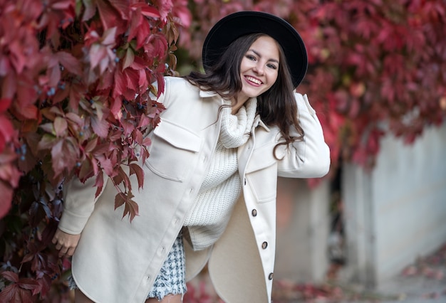 Foto giovane bella ragazza felice in camice bianco e cappello nero. felice autunno.