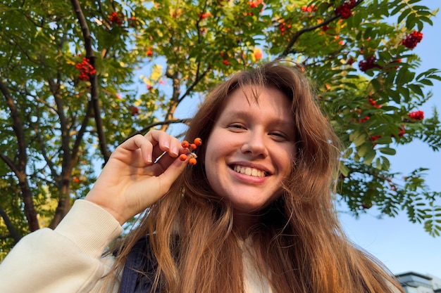 Young happy beautiful woman with branch of ripe rowan in the park