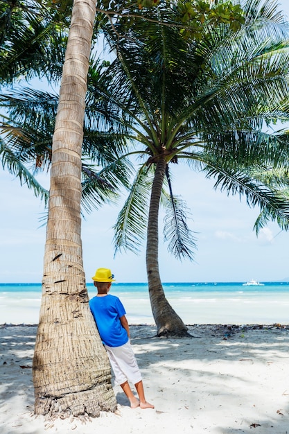 Young happy boy having fun on a white sand tropical beach with palms tree