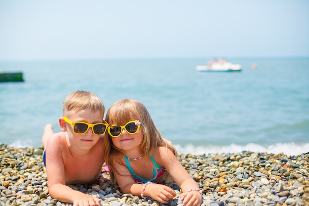 A young happy boy and his little cute sister walking on the sea shore on a warm summer day.