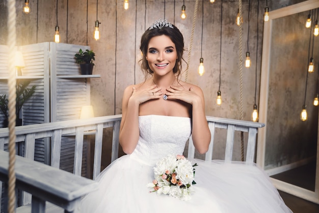 電球の多い部屋で美しい緑豊かなドレスを着ている若い幸せな花嫁