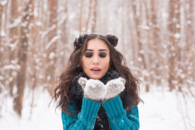 冬の自然の中で雪を吹く若い幸せなブルネットの女性