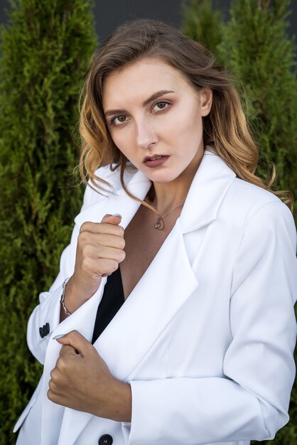 Giovane donna castana felice in vestito bianco che posa alla natura, cedro bianco, ora legale