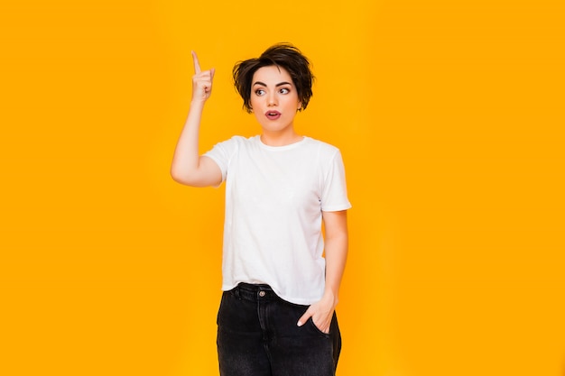 Young happy brunette woman with a short haircut in a white T-shirt on a yellow background. portrait of a young woman with various emotions on a yellow background. space for text