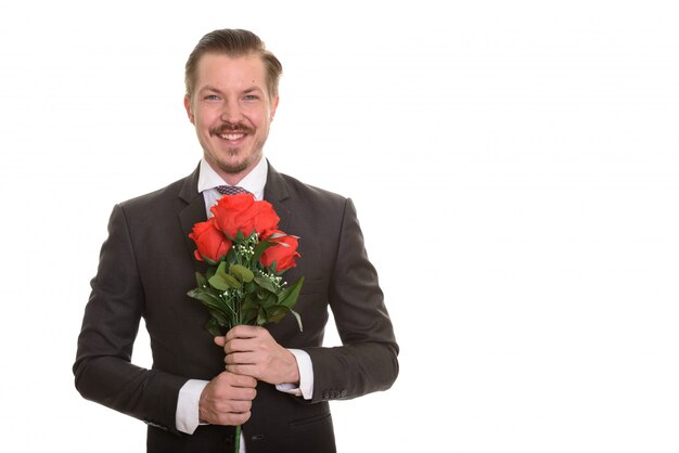 Молодой счастливый бизнесмен держа красные розы готовый на день валентинки